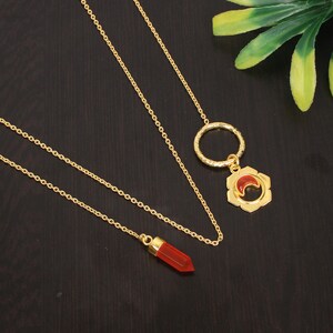 May include: A gold chain necklace with two pendants. One pendant is a red gemstone in a gold setting, the other is a gold circle with a red gemstone in a flower design.