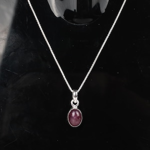 Puede incluir: Un collar de cadena de plata con un colgante con una piedra ovalada de color rosa oscuro.