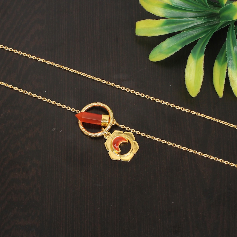 May include: A gold chain necklace with a pendant featuring a red carnelian stone in a circle and a crescent moon design.