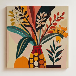 K&ouml;nnte beinhalten: Quadratische Leinwandkunst mit einem lebendigen Blumenarrangement in einer roten Vase mit gelben und braunen Punkten. Das Kunstwerk zeigt eine Mischung aus gr&uuml;nen, orangefarbenen und gelben Bl&auml;ttern und Bl&uuml;ten vor einem cremefarbenen Hintergrund. Das Gem&auml;lde ist an einer wei&szlig;en Wand befestigt.