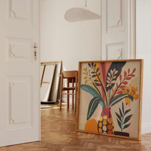 K&ouml;nnte beinhalten: Ein gerahmter Kunstdruck mit einem farbenfrohen Blumenarrangement in einer Vase. Das Kunstwerk zeigt gr&uuml;ne, gelbe, orangefarbene und rote Bl&auml;tter und Bl&uuml;ten. Der Rahmen besteht aus hellem Holz, und der Druck lehnt an einer wei&szlig;en Wand.