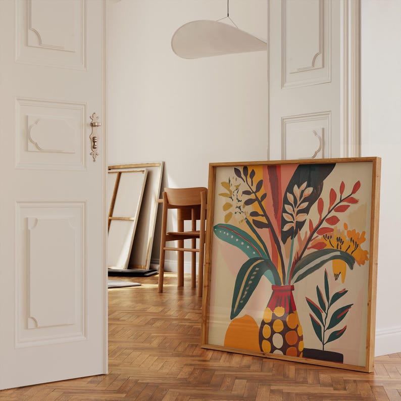 K&ouml;nnte beinhalten: Ein gerahmter Kunstdruck mit einem farbenfrohen Blumenarrangement in einer Vase. Das Kunstwerk zeigt gr&uuml;ne, gelbe, orangefarbene und rote Bl&auml;tter und Bl&uuml;ten. Der Rahmen besteht aus hellem Holz, und der Druck lehnt an einer wei&szlig;en Wand.