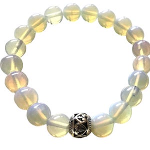 Peut inclure: Un bracelet composé de perles d'opale vert clair et blanc avec un charme argenté au centre.