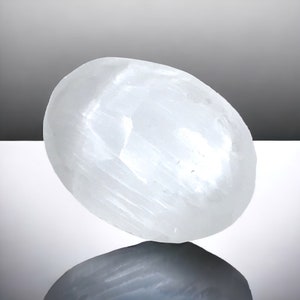 Könnte beinhalten: Ein glatter, weißer Selenitkristall in ovaler Form. Der Kristall hat eine natürliche, polierte Oberfläche und ist eine beliebte Wahl für Meditation und Energieheilung.
