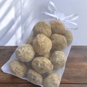 Könnte beinhalten: Ein weißer Netzbeutel gefüllt mit etwa 20 hellbraunen, runden, glatten Steinen. Der Beutel ist mit einem weißen Band gebunden.