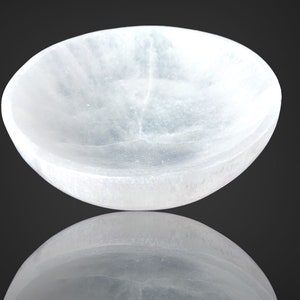 May include: A white selenite bowl with a smooth, polished surface. The bowl is slightly curved and has a reflective surface.