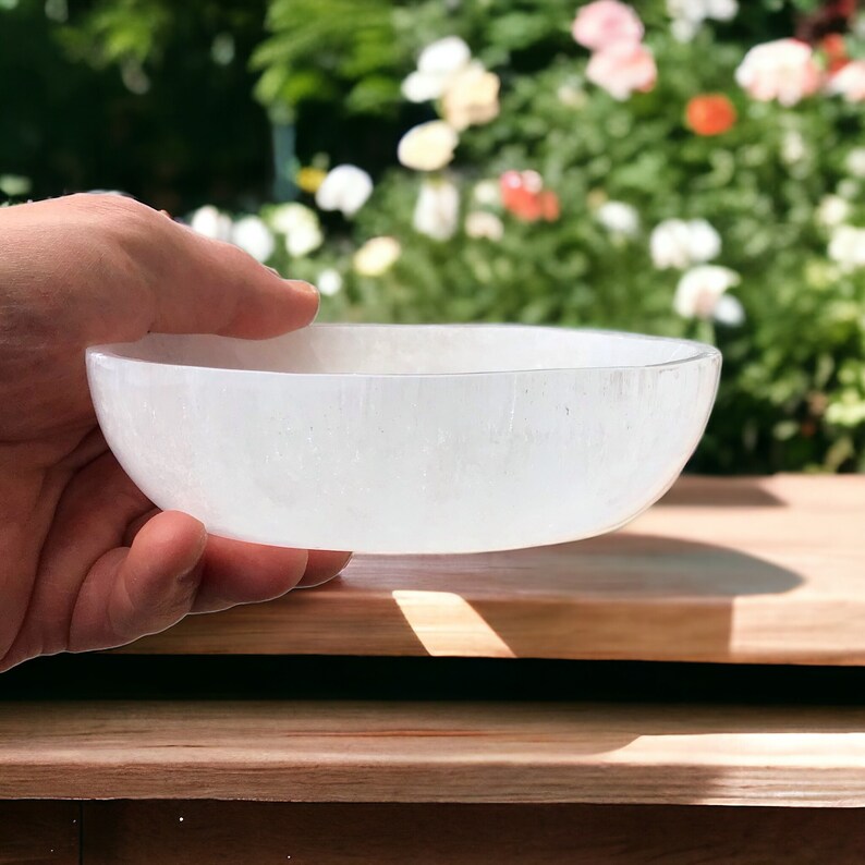 May include: A white selenite bowl, a type of crystal, is held in a hand. The bowl is smooth and has a slightly rounded shape.