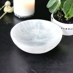 May include: A white selenite bowl with a smooth, polished surface. The bowl is slightly translucent and has a subtle, cloudy appearance.