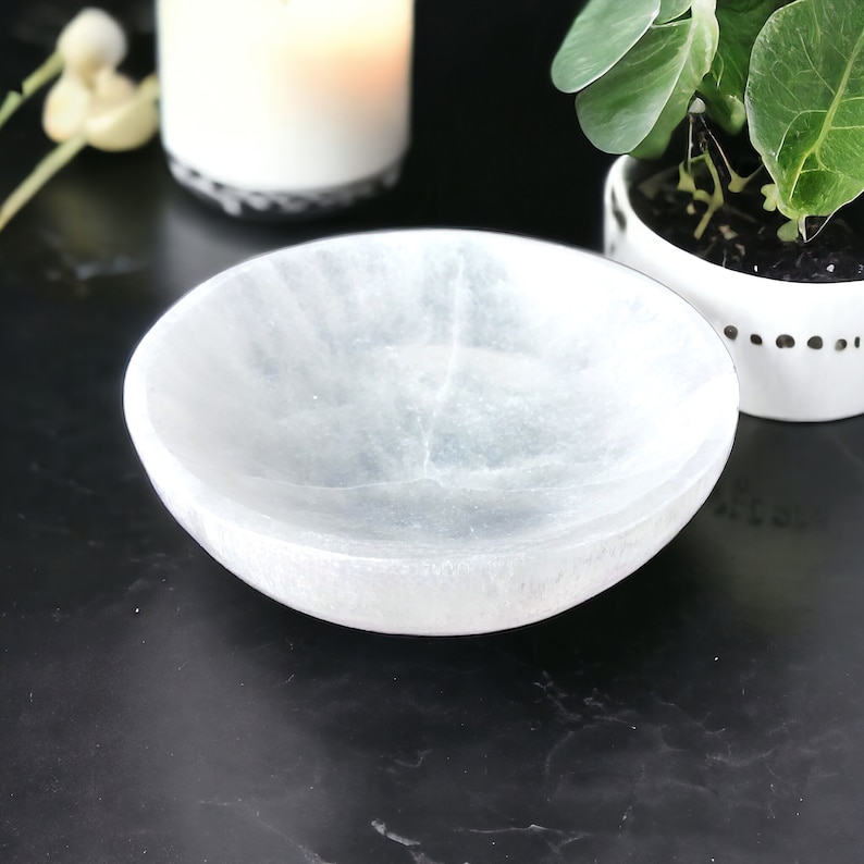 May include: A white selenite bowl with a smooth, polished surface. The bowl is slightly translucent and has a subtle, cloudy appearance.