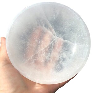 May include: A large, white selenite bowl with a smooth, polished surface. The bowl is slightly translucent and has a few natural cracks.