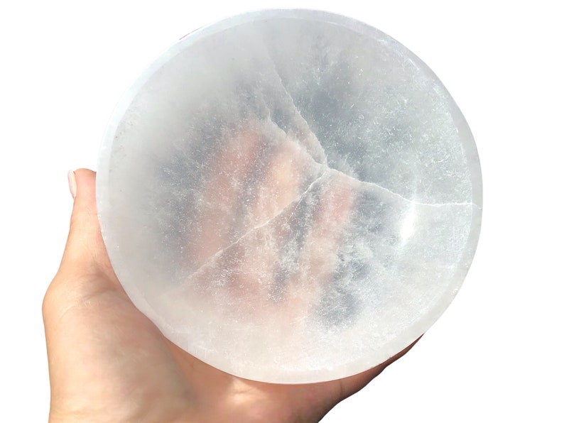 May include: A large, white selenite bowl with a smooth, polished surface. The bowl is slightly translucent and has a few natural cracks.
