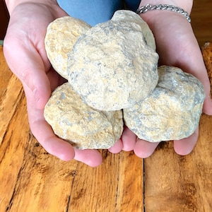 Könnte beinhalten: Eine Sammlung von vier großen, runden, hellbraunen und grauen Geoden. Die Geoden haben eine raue, strukturierte Oberfläche und sind zu einem Stapel angeordnet.