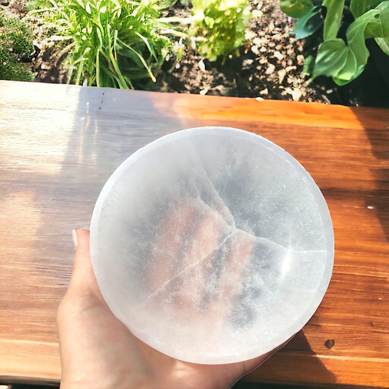 May include: A white selenite bowl with a smooth, polished surface. The bowl is slightly translucent and has a natural crack running through it.