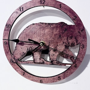 May include: A wooden clock with a brown stain features a silhouette of a bear family walking. The clock face is white with black numbers and hands.