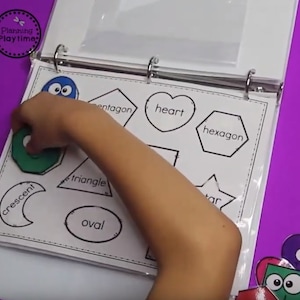 May include: A child's hand places a green pentagon shape onto a white sheet with black outlines of various shapes, including a heart, hexagon, triangle, crescent, oval, and star. The sheet is labeled with the names of each shape.