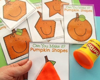 Może przedstawiać: Zestaw zalaminowanych kart zatytułowanych Can You Make it? Pumpkin Shapes przedstawiających różne geometryczne kontury z uśmiechniętymi twarzami dyń, wraz z żółtym pojemnikiem z pomarańczową ciastoliną do zabaw edukacyjnych.