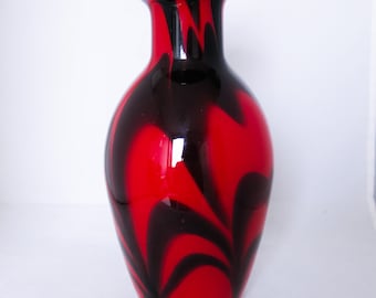 May include: A red and black glass vase with a swirling pattern. The vase has a wide mouth and a narrow neck.