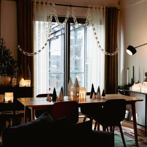 Peut inclure: Int&eacute;rieur chaleureux avec une table &agrave; manger en bois, des chaises et des maisons d&eacute;coratives en papier. Un petit sapin de No&euml;l et des guirlandes lumineuses ajoutent &agrave; l'ambiance festive. La pi&egrave;ce est &eacute;clair&eacute;e par un &eacute;clairage chaleureux.