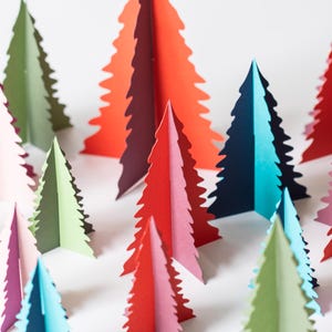 K&ouml;nnte beinhalten: Eine Sammlung farbenfroher Weihnachtsb&auml;ume aus Papier in verschiedenen Rot-, Rosa-, Gr&uuml;n- und Blaut&ouml;nen. Die B&auml;ume sind in einer Gruppe angeordnet, wobei ihre gezackten Kanten eine festliche Darstellung bilden. Die B&auml;ume sind ein dekorativer Artikel.