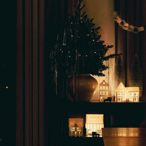 Peut inclure: Sc&egrave;ne de vacances faiblement &eacute;clair&eacute;e avec un petit sapin de No&euml;l dans un vase, des maisons miniatures &eacute;clair&eacute;es et une guirlande en papier. Les maisons ont des fen&ecirc;tres &eacute;clair&eacute;es et une petite voiture jouet devant l'une d'elles.