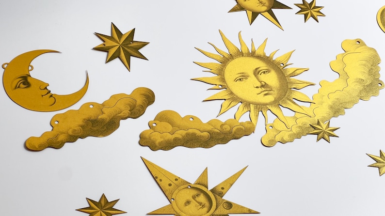 May include: Gold paper cut-outs of a crescent moon, sun, stars, and clouds. The moon, sun, and stars have faces drawn on them.