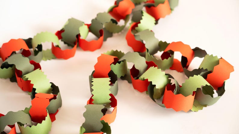 Puede incluir: Una guirnalda de cadena de papel en tonos naranja, verde y gris. Los eslabones est&aacute;n cortados con un borde decorativo, creando una decoraci&oacute;n festiva y colorida. Ideal para fiestas o decoraci&oacute;n de temporada.
