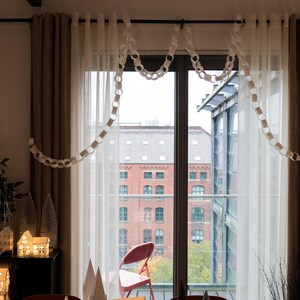 Peut inclure: Int&eacute;rieur d&eacute;cor&eacute; pour les f&ecirc;tes avec une grande fen&ecirc;tre donnant sur une ville. Une guirlande en papier est suspendue &agrave; la fen&ecirc;tre. Des rideaux bruns encadrent la fen&ecirc;tre et un petit sapin de No&euml;l est visible.