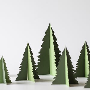 May include: A group of green paper Christmas trees in different sizes. The trees have a jagged edge, mimicking evergreen branches. They are arranged on a white surface, creating a festive, minimalist holiday scene.