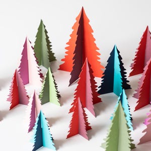 K&ouml;nnte beinhalten: Eine Sammlung bunter Weihnachtsb&auml;ume aus Papier in verschiedenen Rot-, Rosa-, Gr&uuml;n-, Blau- und Lilat&ouml;nen. Die B&auml;ume sind auf einer wei&szlig;en Oberfl&auml;che angeordnet und bilden eine festliche Dekoration. Die B&auml;ume sind etwa 15 cm hoch.