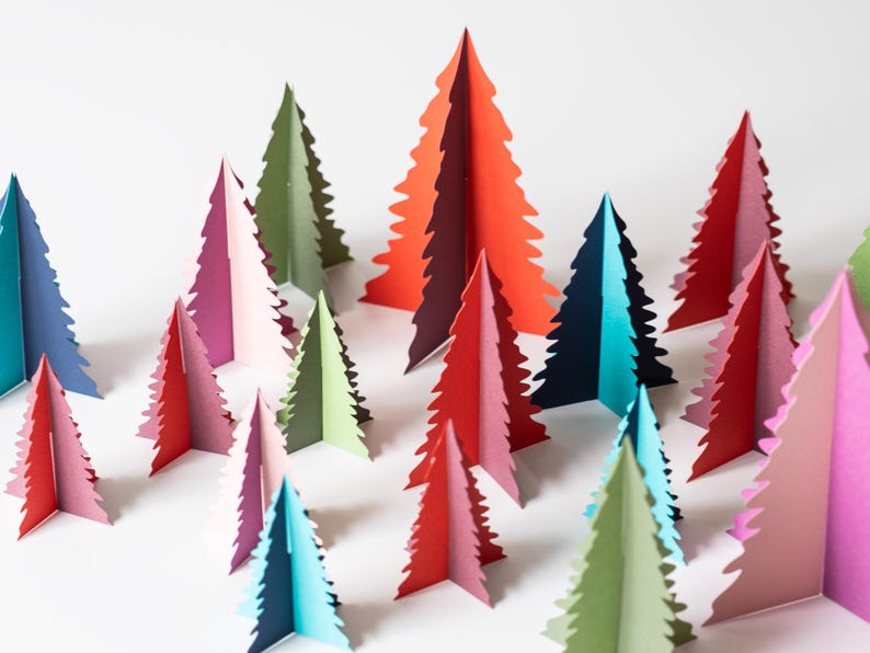K&ouml;nnte beinhalten: Eine Sammlung bunter Weihnachtsb&auml;ume aus Papier in verschiedenen Rot-, Rosa-, Gr&uuml;n-, Blau- und Lilat&ouml;nen. Die B&auml;ume sind auf einer wei&szlig;en Oberfl&auml;che angeordnet und bilden eine festliche Dekoration. Die B&auml;ume sind etwa 15 cm hoch.