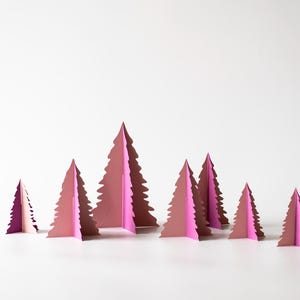 K&ouml;nnte beinhalten: Eine Sammlung rosa Weihnachtsb&auml;ume aus Papier in verschiedenen Gr&ouml;&szlig;en. Die B&auml;ume sind in einer Gruppe angeordnet, mit wei&szlig;em Hintergrund. Die B&auml;ume haben ein geschichtetes Design und erzeugen einen 3D-Effekt.