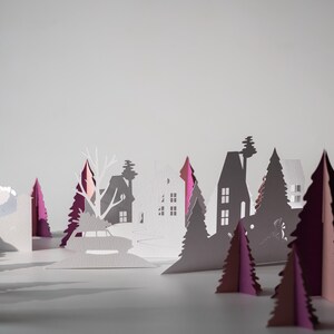 K&ouml;nnte beinhalten: Eine Papier-Winterlandschaft mit wei&szlig;en H&auml;usern, B&auml;umen und einem Auto mit einem Weihnachtsbaum. Die B&auml;ume sind wei&szlig; und magenta und erzeugen einen geschichteten, dreidimensionalen Effekt vor einem hellgrauen Hintergrund.