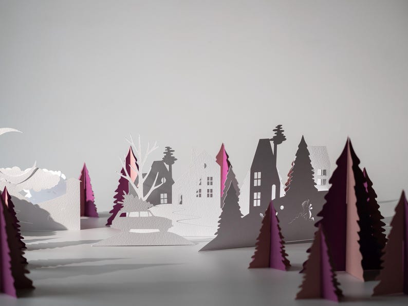 K&ouml;nnte beinhalten: Eine Papier-Winterlandschaft mit wei&szlig;en H&auml;usern, B&auml;umen und einem Auto mit einem Weihnachtsbaum. Die B&auml;ume sind wei&szlig; und magenta und erzeugen einen geschichteten, dreidimensionalen Effekt vor einem hellgrauen Hintergrund.