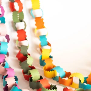 Puede incluir: Primer plano de guirnaldas de cadenas de papel de colores. Las cadenas est&aacute;n hechas de bucles de papel unidos en tonos de rosa, morado, verde azulado, verde, rojo, naranja, amarillo y blanco. Ideal para decoraciones de fiestas o proyectos de manualidades.