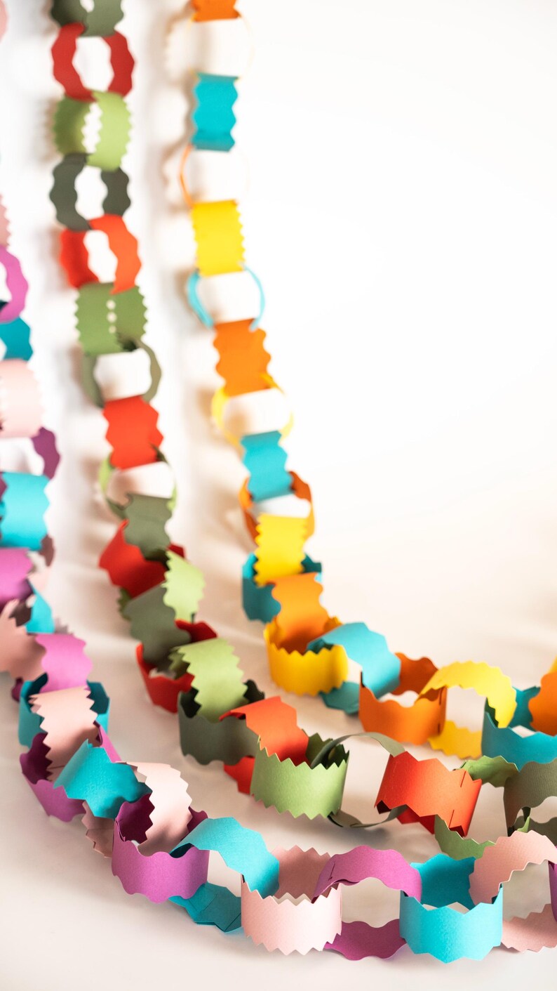 Puede incluir: Primer plano de guirnaldas de cadenas de papel de colores. Las cadenas est&aacute;n hechas de bucles de papel unidos en tonos de rosa, morado, verde azulado, verde, rojo, naranja, amarillo y blanco. Ideal para decoraciones de fiestas o proyectos de manualidades.