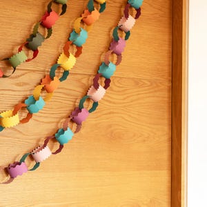 Puede incluir: Guirnalda de cadena de papel colorida en tonos rojo, verde, amarillo, naranja, azul y rosa, colgada en una puerta de madera clara. Los eslabones de papel est&aacute;n cortados con un borde decorativo, creando un aspecto festivo y l&uacute;dico. Ideal para decoraciones de fiesta.