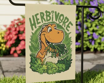 May include: A garden flag with a cartoon dinosaur eating green plants. The flag is beige with green and brown accents. The text "Herbivore" is printed in black letters.