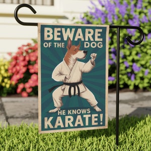 May include: A garden flag featuring a cartoon dog in a white karate uniform with a black belt. The flag has a blue background with the text "Beware of the Dog He Knows Karate!" in white.