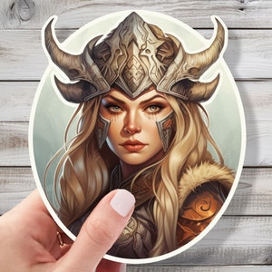 May include: A woman with long blonde hair wears a silver helmet with horns and a fur-trimmed shoulder piece. Her eyes are blue and she has a serious expression.
