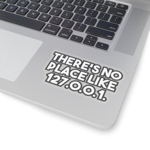 Könnte beinhalten: Ein weißer Aufkleber mit schwarzem Text, der "THERE'S NO PLACE LIKE 127.0.0.1." lautet, ist auf einem silbernen Laptop angebracht. Der Aufkleber hat einen schwarzen Rand und befindet sich auf der unteren rechten Seite des Laptops.