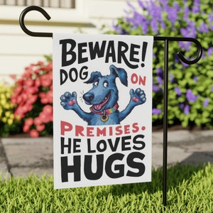 Puede incluir: Una bandera de jardín blanca con un perro de dibujos animados azul con un collar arcoíris. La bandera dice "¡Cuidado! Perro en la propiedad. Le encantan los abrazos."