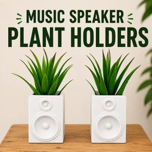 May include: Two white rectangular plant holders shaped like music speakers, each containing a green artificial succulent plant. The text MUSIC SPEAKER PLANT HOLDERS is printed in dark green above the two white speaker-shaped planters.