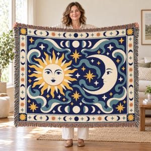 Peut inclure: Un plaid tissé présentant un fond bleu foncé avec un soleil jaune central et un croissant de lune crème, tous deux dotés de traits de visage. Le motif comprend des nuages bleu sarcelle tourbillonnants, des étoiles jaunes et une bordure de phases lunaires.