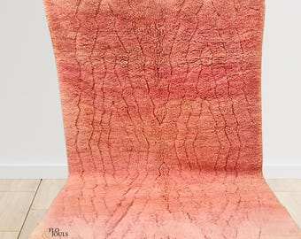 May include: A pink and white Moroccan rug with a geometric pattern. The rug has a fringe border and is made of wool.