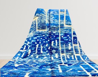 Puede incluir: Una alfombra marroquí azul y blanca con un patrón geométrico. La alfombra tiene un borde de flecos y está doblada por la mitad.