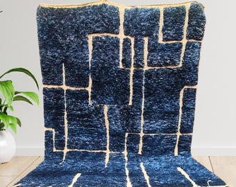 Puede incluir: Una alfombra geométrica azul y blanca con borde de flecos. La alfombra tiene un diseño moderno con un patrón abstracto audaz.