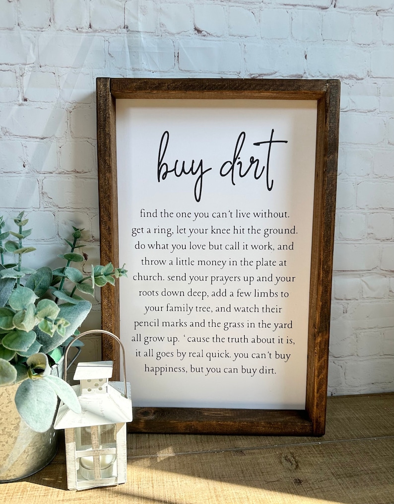 May include: A wooden sign with the text "buy dirt" and a quote about finding love and happiness. The sign is on a white background and has a rustic brown frame.