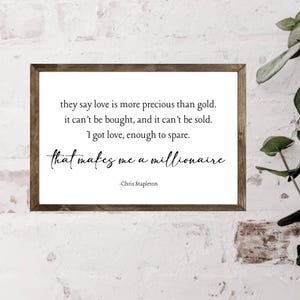 May include: A framed wooden sign with a white background and black text. The text reads, "they say love is more precious than gold. it can't be bought, and it can't be sold. I got love, enough to spare. that makes me a millionaire -Chris Stapleton."