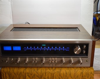 May include: A vintage Pioneer stereo receiver with a silver face, wood cabinet, and blue illuminated display. It features multiple knobs and buttons for audio control. The receiver is a classic piece of audio equipment.
