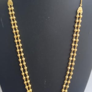May include: A double-strand gold necklace featuring small, textured, spherical beads arranged in two parallel rows. The necklace connects at the top with triangular metal findings on each side, leading to a thin, smooth gold chain that extends upward.